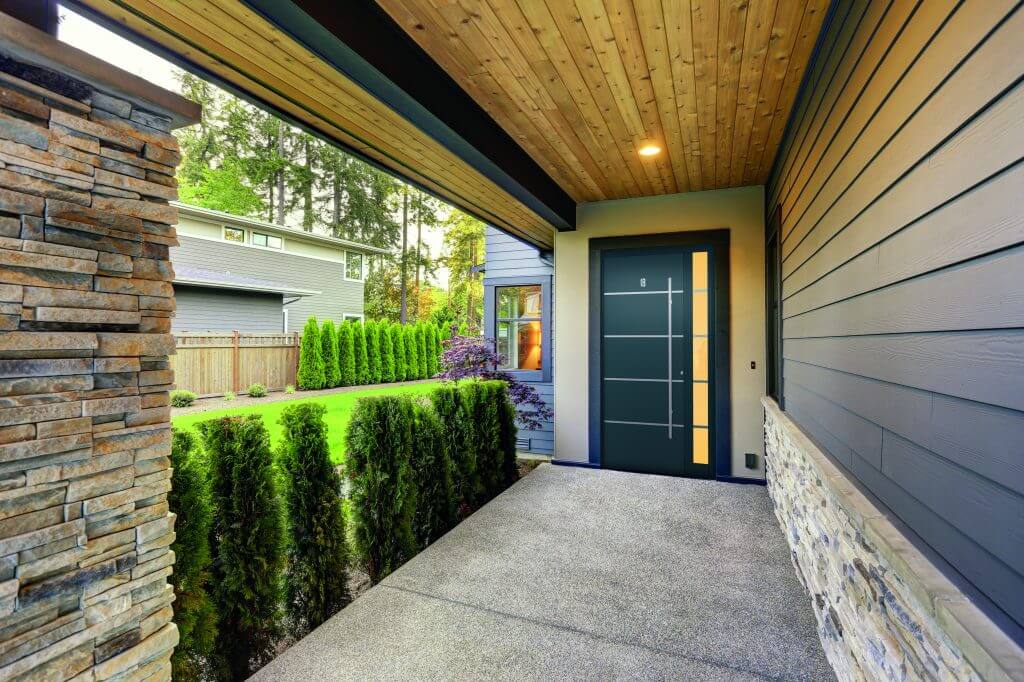 shot of black composite door with pull bar next to garden under a porch